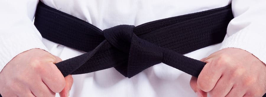 A person tightening a black belt, symbolizing shodan rank, used metaphorically in Go to indicate reaching the first dan level.