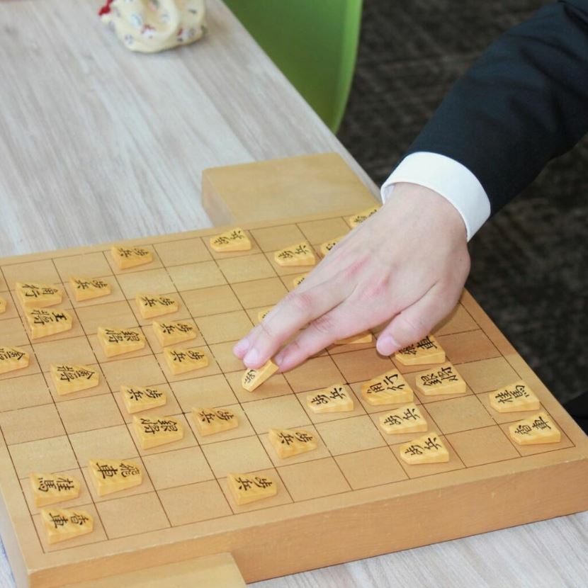 A close-up of a Shogi (Japanese chess) board with a person moving a piece.