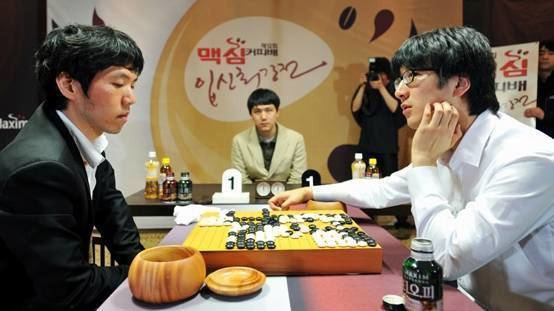 Lee Changho playing a competitive Go match, facing an opponent across the board, with an official watching in the background.