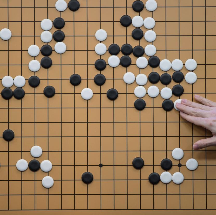 A close-up of a Go board with black and white stones placed strategically, and a hand making a move.