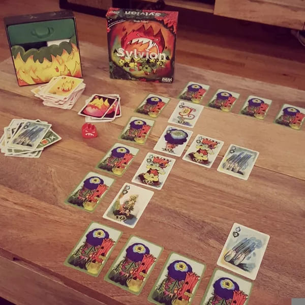 Sylvion card game displayed with neatly arranged cards, dice, and the game box featuring a fiery creature illustration.