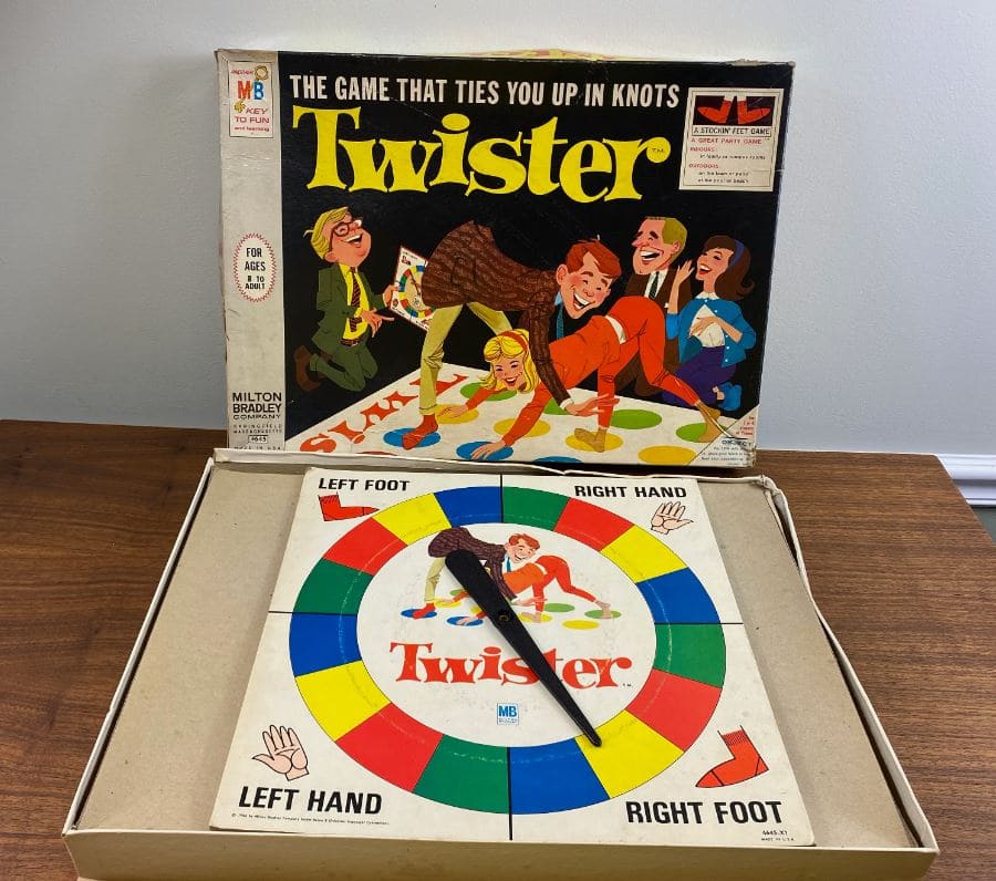 A 1990s version of the classic Twister game, featuring a colorful spinner and original game box with playful illustrations of people playing.