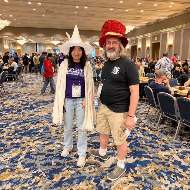 Audrey Wang in a white wizard hat and Trevor Morris in a red top hat, standing together in the Congress playing hall.
