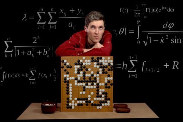 A man leaning on a Go board surrounded by math formulas on a blackboard