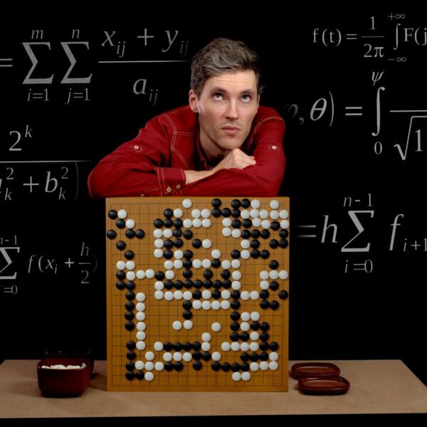 A man leaning on a Go board surrounded by math formulas on a blackboard