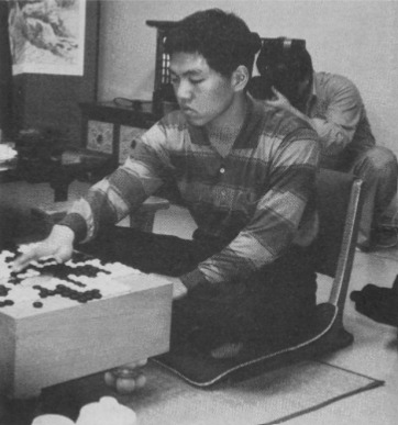 A young Lee Changho sitting on the floor, deeply focused as he practices Go, with a traditional Go board in front of him.